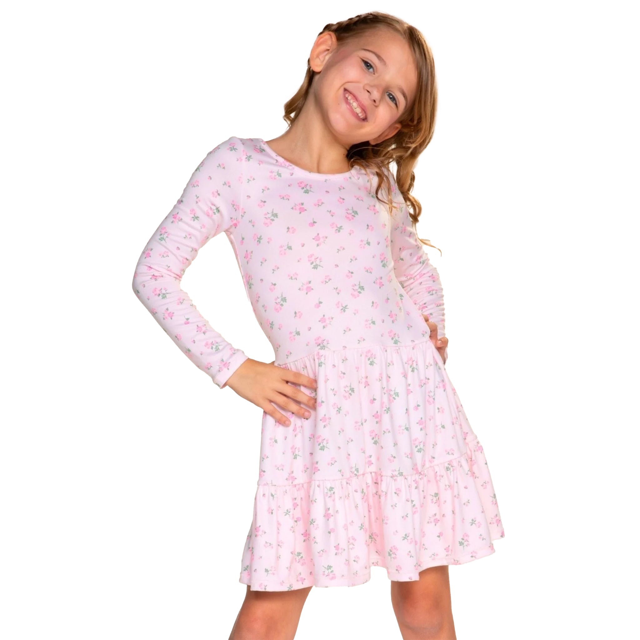 A young girl with light brown hair wearing a light pink long-sleeve tiered dress with a small floral print, posing against a solid white background.