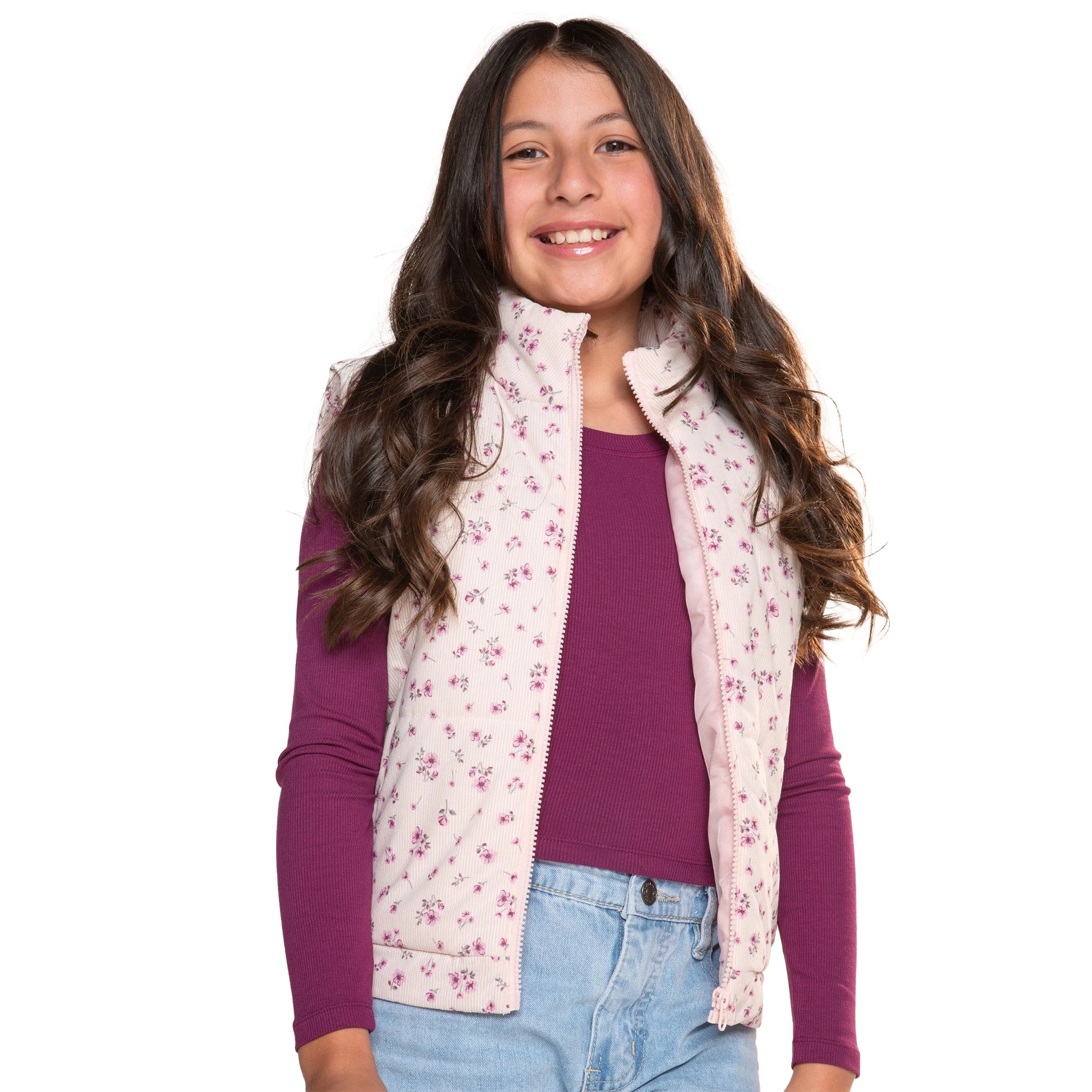 A young girl with long brown hair smiling, wearing a light pink floral zip-up vest over a dark purple long-sleeve shirt and light blue jeans, against a solid white background.