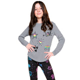 A young girl with long brown hair stands against a white background wearing a heather gray long-sleeve shirt with colorful graphic prints (star, heart, rainbow, 'LOVE' text) and black leggings with a colorful pattern.