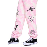 Pink and white tie-dye jogger pants with black graphic prints including hearts, a rainbow, a star, and the word 'LOVE' with arrows, shown on a child's legs with black Converse sneakers against a white background.