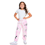 A young girl modeling pink and white tie-dye sweatpants with black doodle graphics, paired with a light gray t-shirt and white sneakers, against a solid white background.