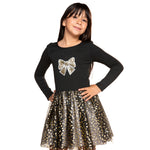 A young girl modeling a black long-sleeve top with a glittery gold bow graphic on the chest, paired with a black and gold glittery tutu skirt, against a plain white background.
