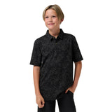 A young boy modeling a black short-sleeve button-up shirt with a subtle light gray leaf pattern, paired with black pants, against a solid white background.