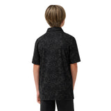 A child viewed from the back wearing a short-sleeve button-up shirt with a dark base and a subtle light floral or leafy pattern, paired with dark pants, against a plain white background.
