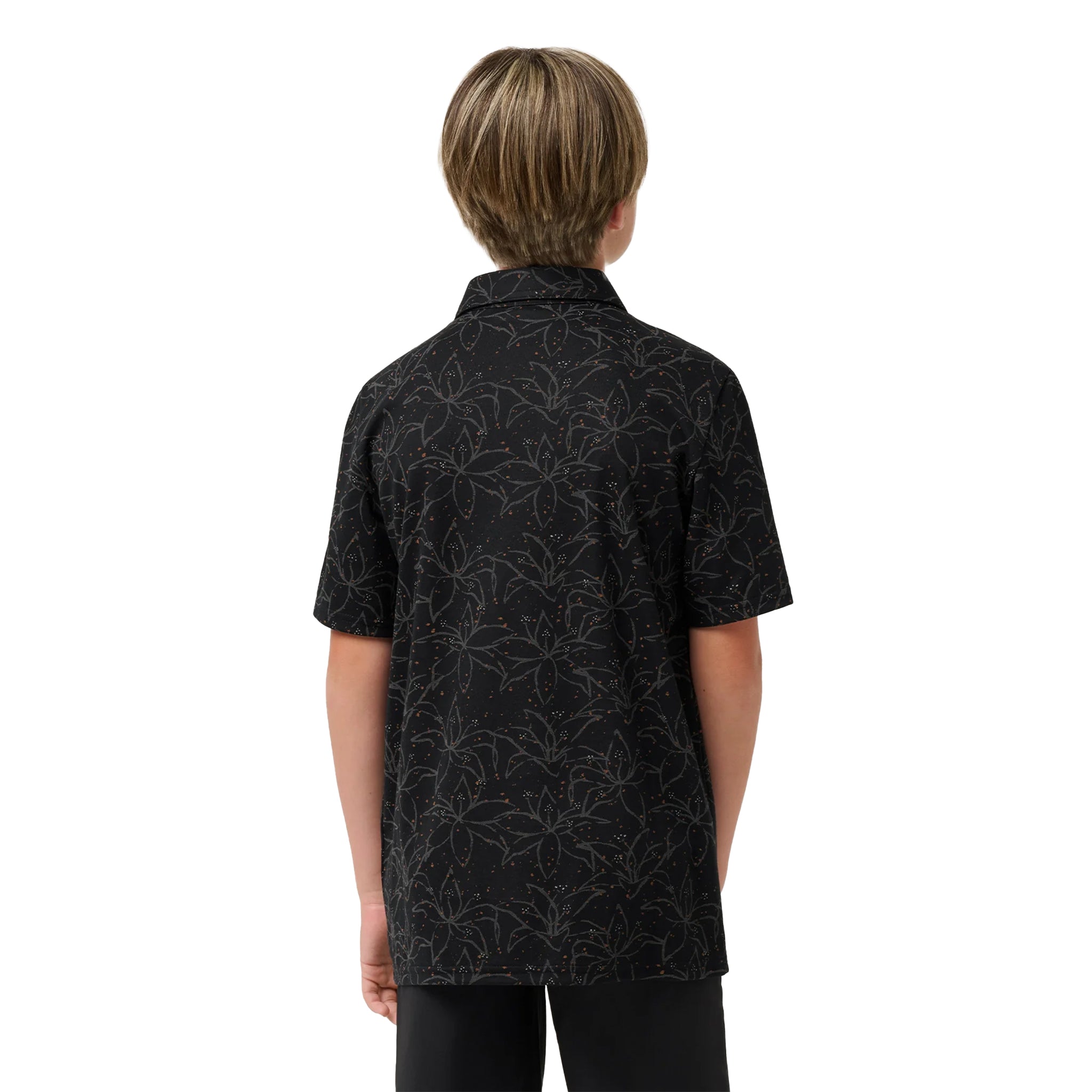 A child viewed from the back wearing a short-sleeve button-up shirt with a dark base and a subtle light floral or leafy pattern, paired with dark pants, against a plain white background.