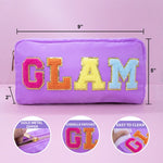 Purple zippered cosmetic pouch with large glittery 'GLAM' lettering in pink, orange, yellow, and blue on the front. Black dimension lines show 9 inches wide, 5 inches tall, and 2 inches deep, with three circular inset detail images at the bottom showing a gold zipper, chenille patches, and easy cleaning.