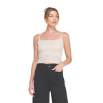A woman modeling a beige ribbed knit camisole top with thin spaghetti straps against a solid white background.