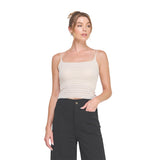 A woman modeling a beige ribbed knit camisole top with thin spaghetti straps against a solid white background.