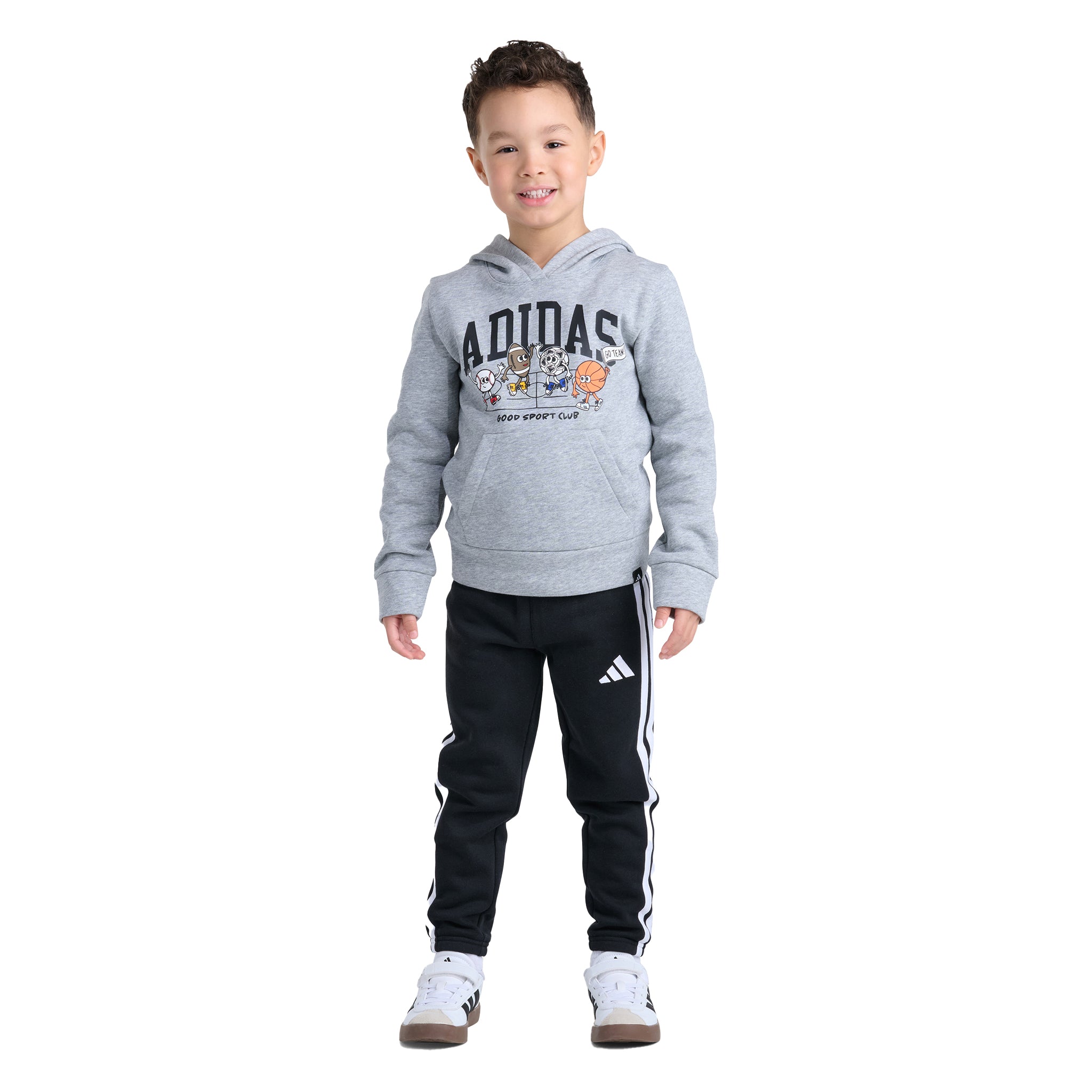 A young boy modeling a gray Adidas hoodie with a cartoon graphic and black Adidas track pants with white stripes, set against a plain white background.