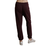 A person shown from the waist down wearing dark burgundy jogger sweatpants and white sneakers against a plain white background.
