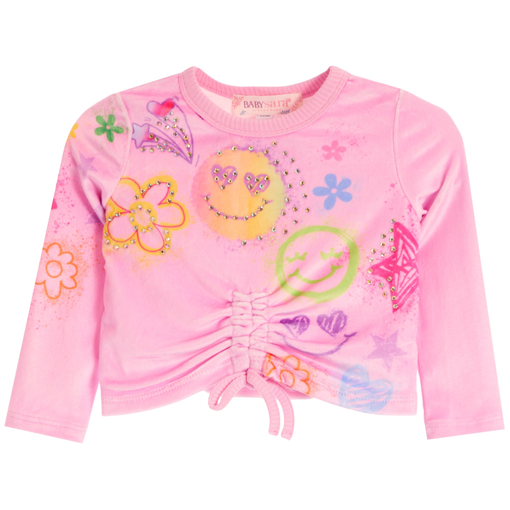 A pink long-sleeve crop top for kids, featuring a front drawstring tie and an all-over colorful graphic print with smiley faces, flowers, stars, and hearts. 