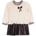 A girls' long-sleeve knit top and pleated skirt set in cream and black. The cream cable-knit top features a striped crew neck, striped cuffs, a ruffled hem, and a black sequined bow on the chest.