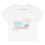 A white short-sleeve crewneck t-shirt by Katie J, featuring a vintage postage stamp graphic on the front with a coastal landscape, shells, and a stamp cancellation mark.