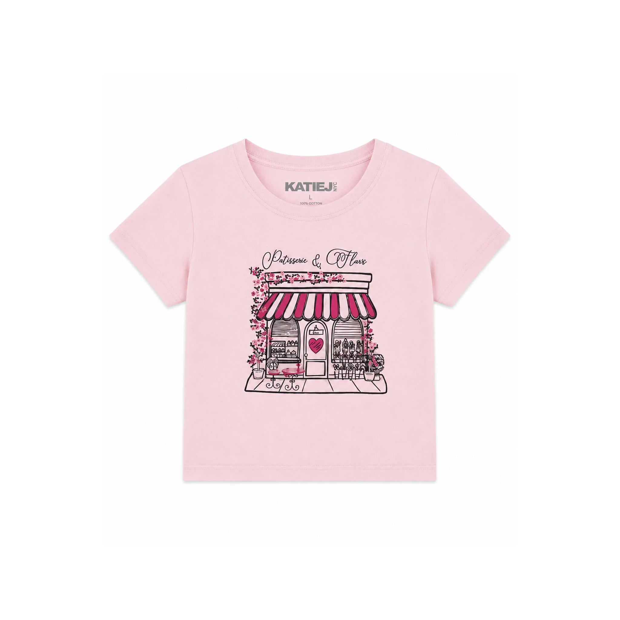 A light pink short-sleeve t-shirt for kids by Katie J, featuring a graphic print of a Parisian-style boutique with red and white striped awning, pink flowers, and a heart on the front.