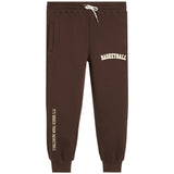 Dark brown sweatpants with white drawstrings, featuring 'BASKETBALL' printed in white on the upper right thigh and 'IT'S BIGGER THAN BASKETBALL' printed vertically in white on the lower left leg.