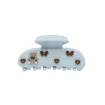 A light blue hair claw clip decorated with small brown enamel accents, including a teddy bear, bows, and hearts, shown against a plain white background.