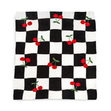 A square textile item, likely a napkin or small towel, featuring a black and white checkered pattern with embroidered red cherries and green leaves scattered across it, shown flat against a white background.