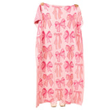 A pink blanket with a repeating bow pattern, hanging against a plain white background.