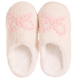 A pair of fluffy off-white slip-on slippers with a light pink bow design embellished with small white pearls on the top, shown against a plain white background.