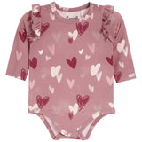 A dusty rose pink long-sleeve baby bodysuit with an all-over heart pattern in shades of red, pink, and white, featuring ruffle details on the shoulders and snap closures at the crotch and neckline.