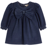 A toddler girl's navy blue denim long-sleeve top featuring a large matching fabric bow at the neckline and ruffled cuffs, shown against a plain white background.