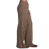 Side view of a person wearing leopard-print wide-leg pants with a white drawstring, paired with brown shoes, against a plain white background.