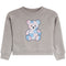 A heather gray long-sleeve crewneck sweatshirt for toddlers, featuring a central patchwork teddy bear graphic in pastel pink and blue tones.