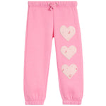 Pink sweatpants with three light pink heart patches decorated with tiny floral details, arranged vertically on the left leg. The pants feature an elastic waistband with a matching drawstring and elastic cuffs at the ankles.