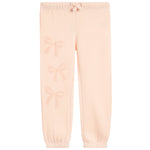 Light peach pink sweatpants with a subtle tonal bow pattern printed down the left leg, featuring an elastic waistband with a drawstring and elastic cuffs.