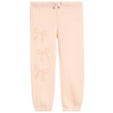 Light peach pink sweatpants with a subtle tonal bow pattern printed down the left leg, featuring an elastic waistband with a drawstring and elastic cuffs.