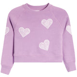 A lavender purple cropped crewneck sweatshirt with white embroidered lace-patterned hearts scattered across the front and sleeves, shown against a plain white background.