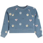 A dusty blue cropped sweatshirt with an all-over print of smiley faces, hearts, and simple smiley faces in pink, white, and yellow.