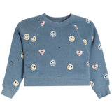 A dusty blue cropped sweatshirt with an all-over print of smiley faces, hearts, and simple smiley faces in pink, white, and yellow.