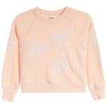 A light peach-pink crewneck sweatshirt featuring embroidered white bow patterns on the front and sleeves, displayed against a solid white background.