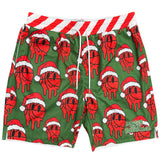 Green swim trunks with an all-over red basketball wearing a Santa hat pattern, a red and white striped waistband, and white drawstrings. A green 'Bigger Than Basketball' logo is printed on the lower right leg.