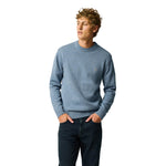 A man wearing a light blue crewneck knit sweater and dark jeans, standing against a solid white background.
