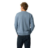 A man with curly brown hair is shown from behind wearing a light blue knit sweater and dark blue jeans against a solid white background.
