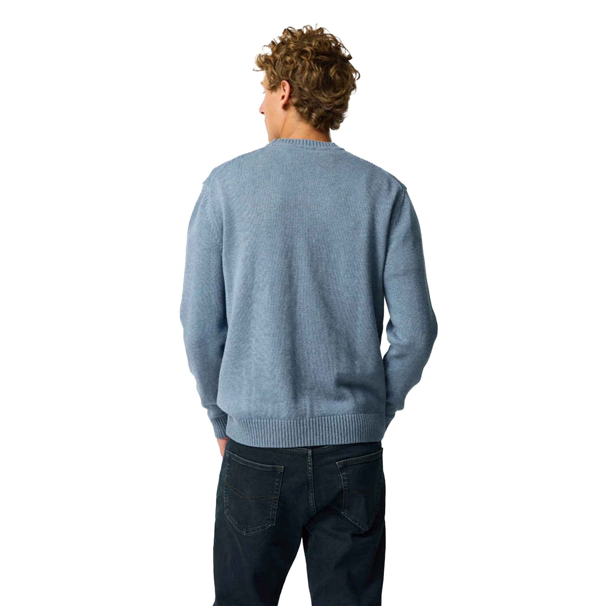 A man with curly brown hair is shown from behind wearing a light blue knit sweater and dark blue jeans against a solid white background.