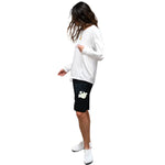 A woman modeling a white long-sleeve t-shirt and black athletic shorts with a white graphic logo, set against a plain white background.