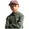 A child wearing a dark olive green Nike hoodie with a white logo on the chest, paired with a dusty rose Nike cap, set against a plain white background.