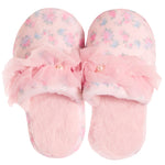 A pair of pink slip-on slippers with a soft floral pattern, featuring a large ruffled pink bow across the top with small pearl-like accents, set against a plain white background.