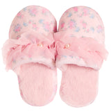 A pair of pink slip-on slippers with a soft floral pattern, featuring a large ruffled pink bow across the top with small pearl-like accents, set against a plain white background.