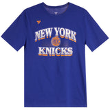 A royal blue short-sleeve t-shirt featuring 'NEW YORK KNICKS' printed in white and orange arched text across the chest, with a basketball graphic in the center and a small orange logo on the left chest.