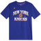 A royal blue short-sleeve t-shirt featuring 'NEW YORK KNICKS' printed in white and orange arched text across the chest, with a basketball graphic in the center and a small orange logo on the left chest.