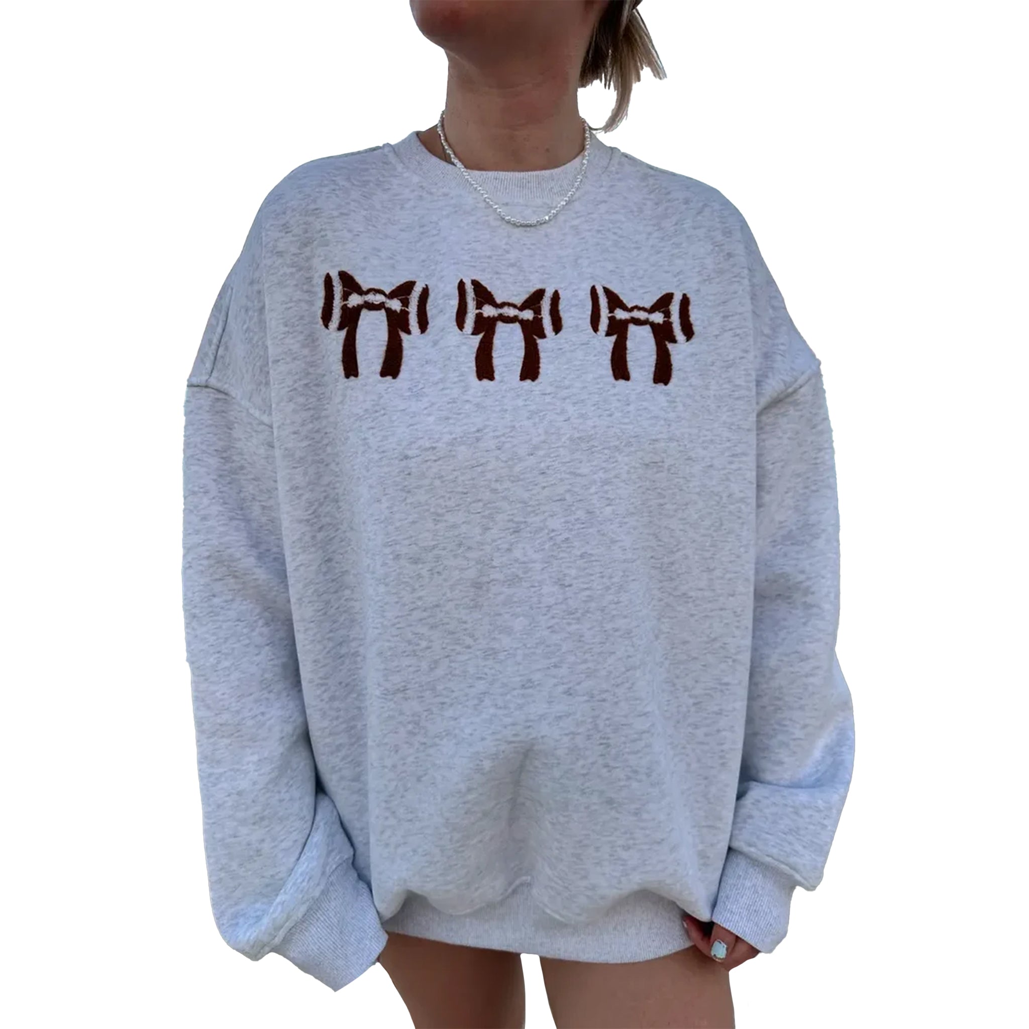 A person wearing an oversized light heather gray sweatshirt with three dark brown bow graphics across the chest, shown against a plain white background.