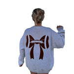 A woman viewed from behind wearing a light heather gray sweatshirt with a large brown and white football-and-bow graphic printed on the back.