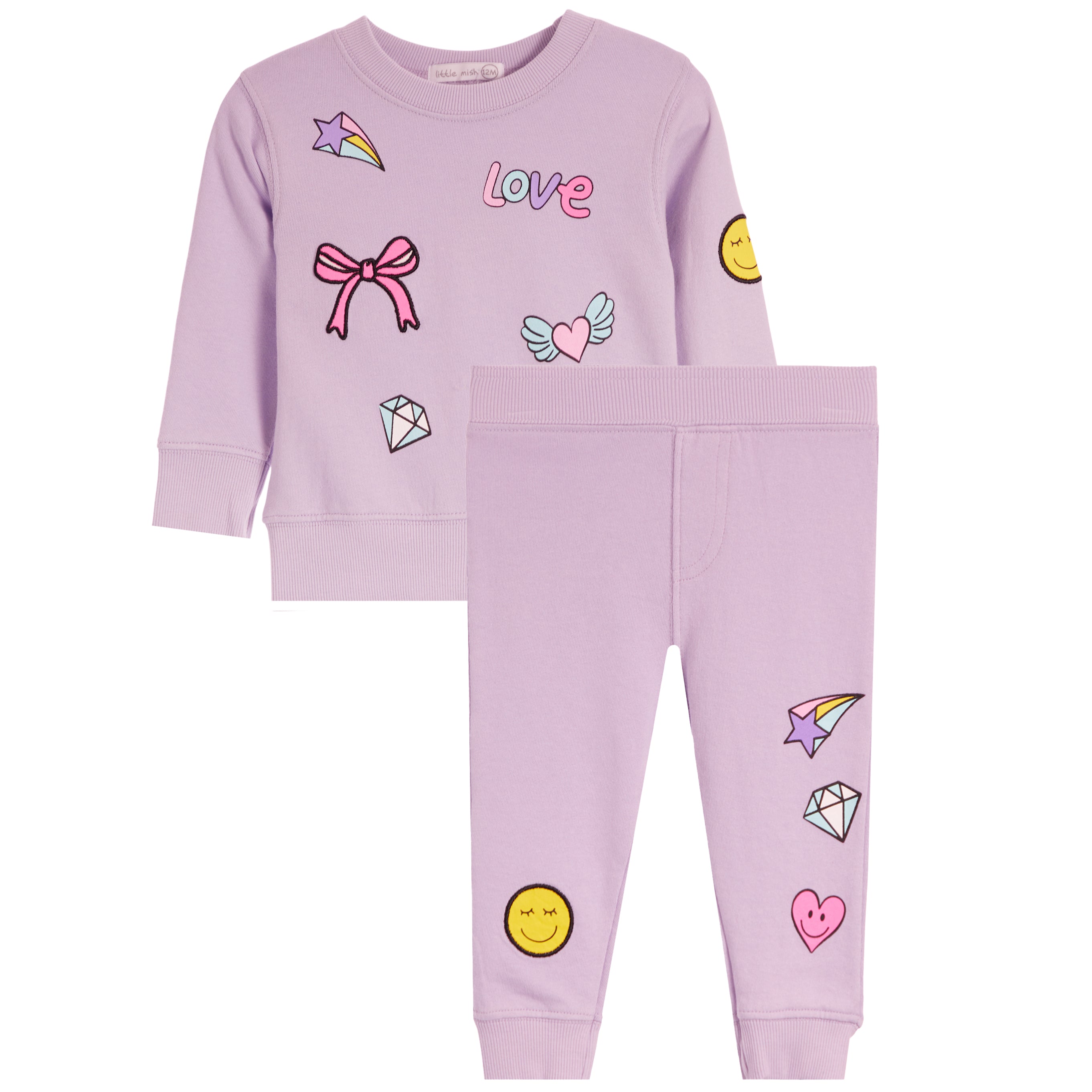 Two-piece set in light lavender purple, featuring a long-sleeve sweatshirt and matching pants. The set is decorated with cute cartoon graphics including a pink bow, a pink heart with wings, a yellow smiley face, a diamond, and a star w rainbow.