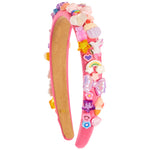 A pink headband decorated with colorful, whimsical charms including a rainbow, unicorn, cupcakes, stars, and bows, shown against a plain white background.