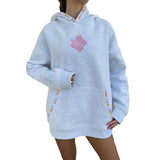 A person wearing an oversized light grey heather hoodie with a pink flower graphic on the chest, multicolored dotted trim along the hood and pockets, and a front kangaroo pocket, shown against a plain white background.