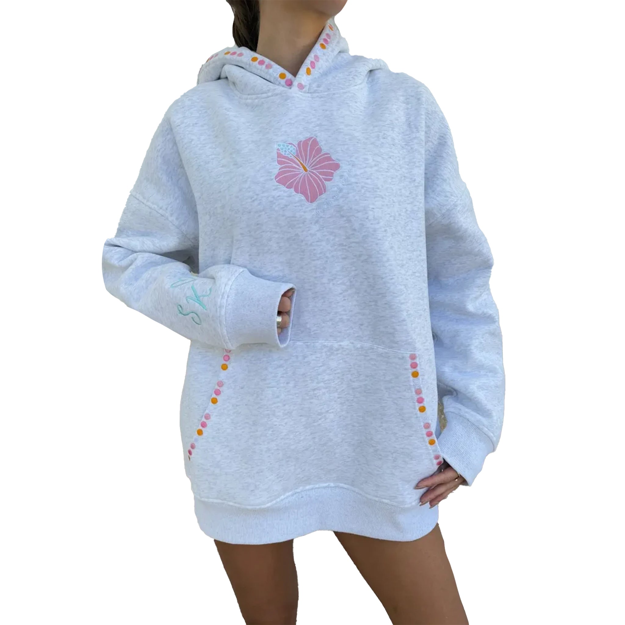 A person wearing an oversized light grey heather hoodie with a pink flower graphic on the chest, multicolored dotted trim along the hood and pockets, and a front kangaroo pocket, shown against a plain white background.